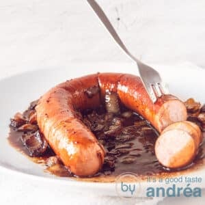A square photo with a smoked sausage on a white plate with a soy sauce around it. A fork pierces it.