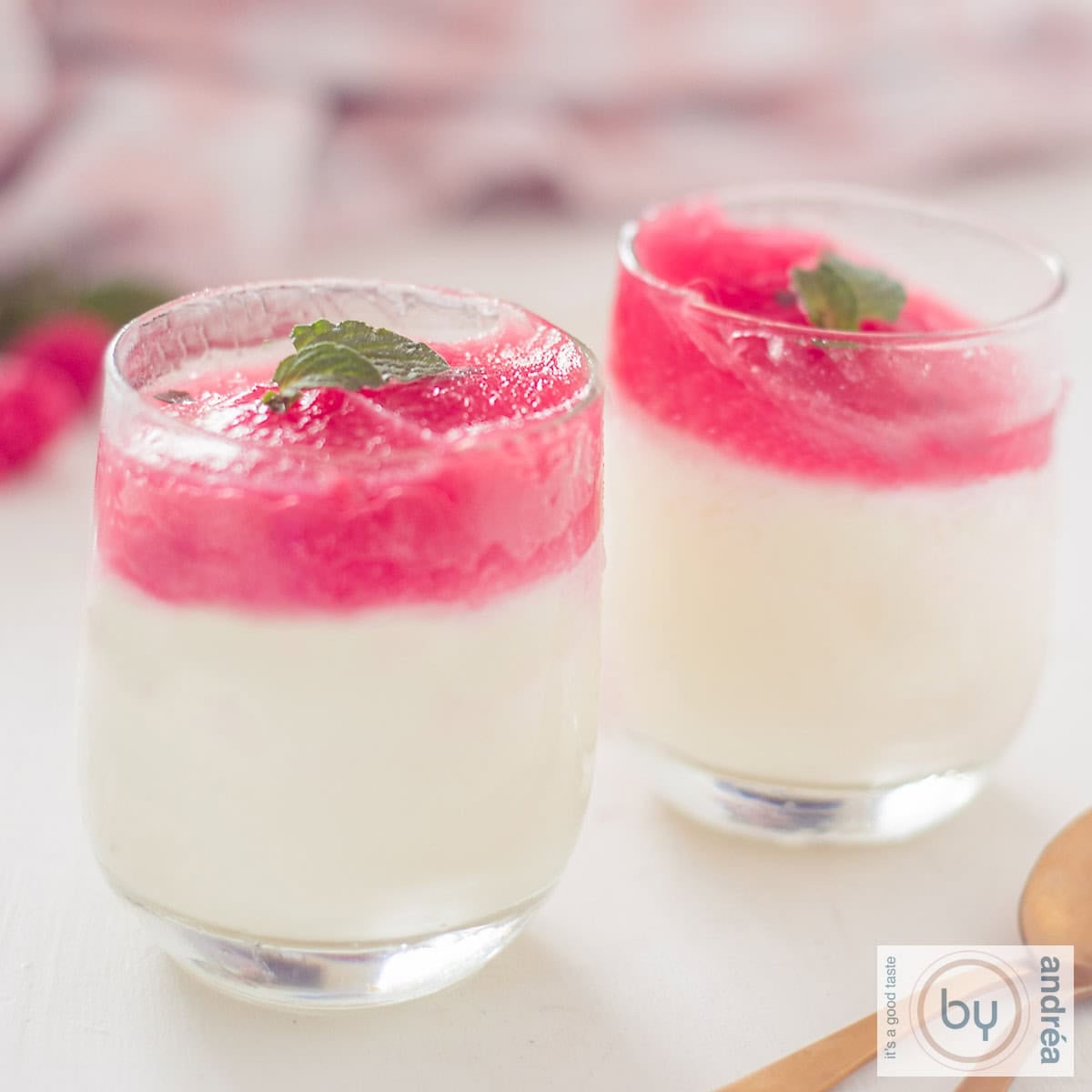 A square photo of two glasses filled with lime yogurt ice cream with a raspberry and mint glaze. The background is white.