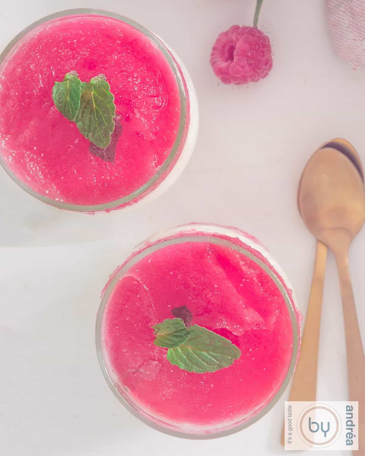 Een foto van bovenaf van een toetje met yoghurtijs met frambozengelei topping met munt.