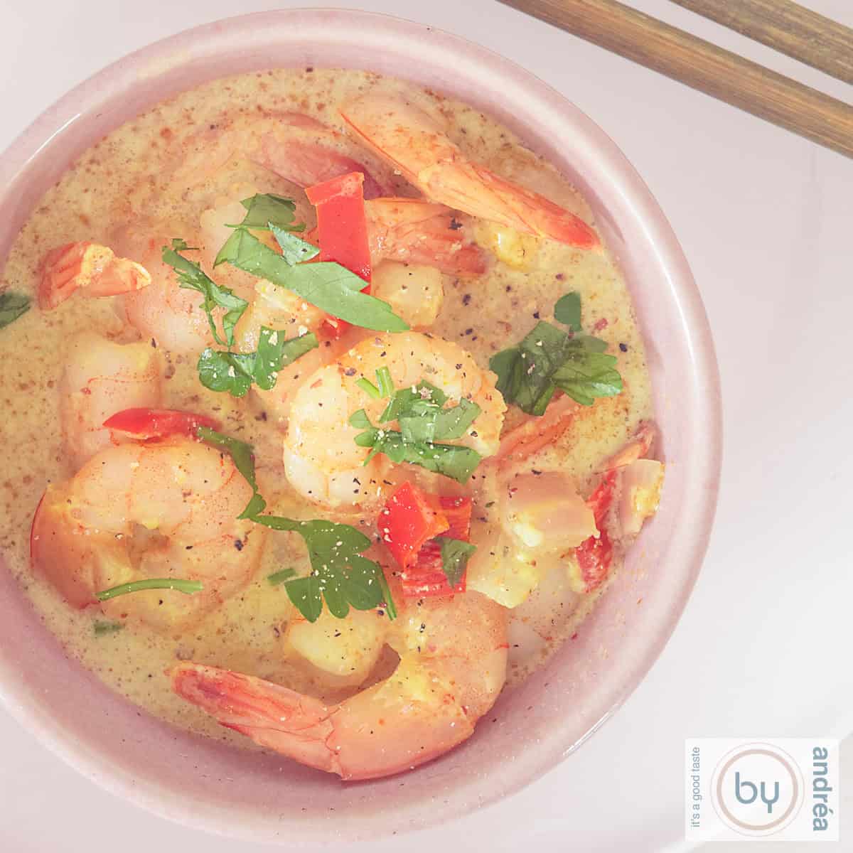 A square photo of a pink bowl photographed from above filled with shrimp curry in coconut milk.