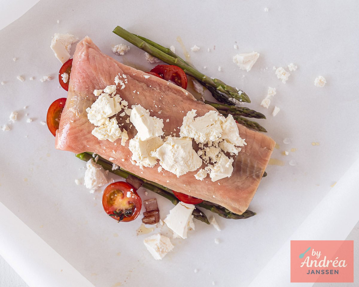 A baking paper with asparagus, cherry tomatoes, salmon and feta cheese.