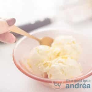 A square photo with homemade lemon ice cream in an orange bowl. A spoon takes a bite. A grater in the background