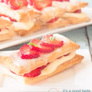 A puff pastry strawberry pastry on a white plate and a blue background. There are more in the background