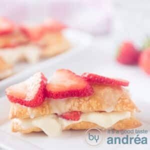 A square photo with a strawberry tompouce with strawberries on top. More tompouces in the background.