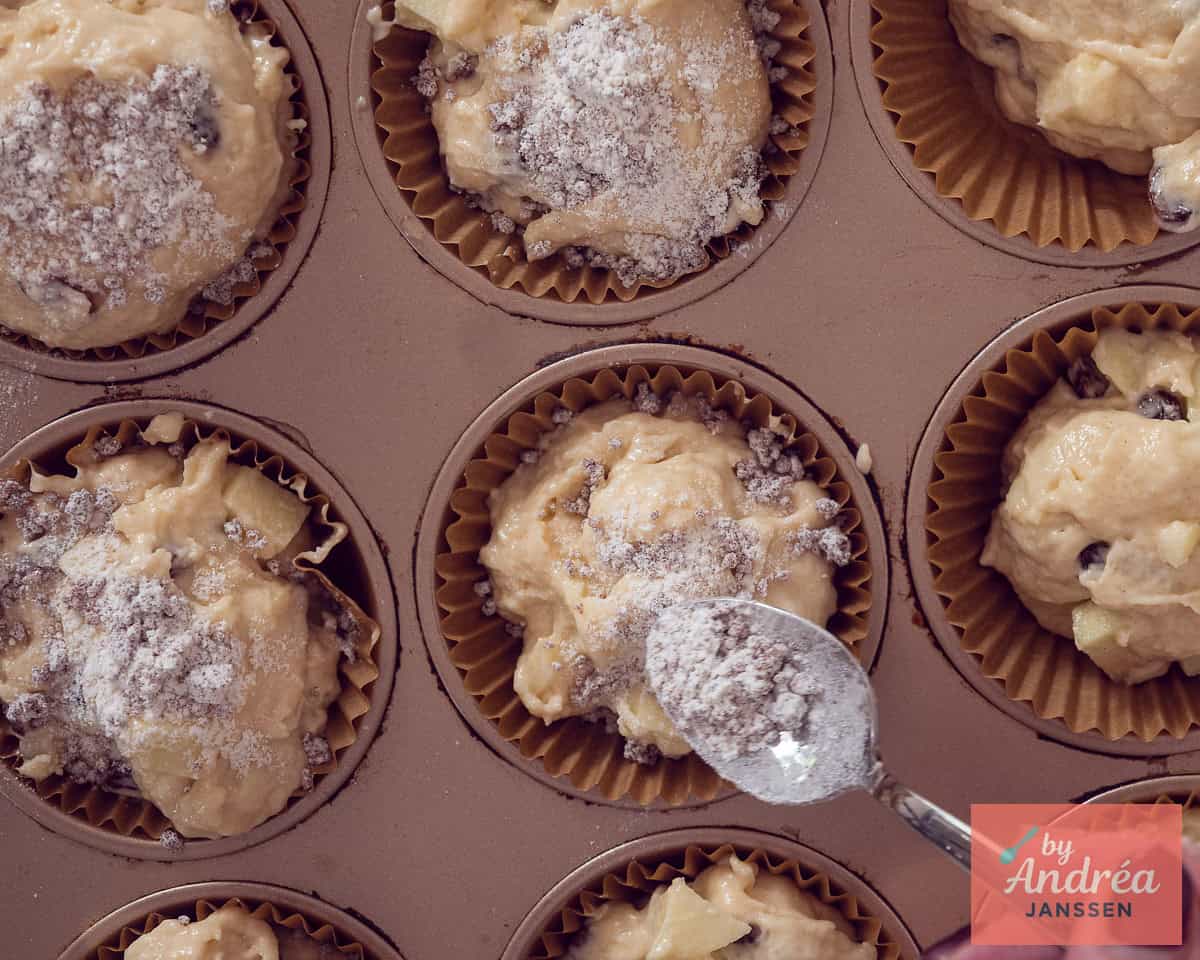 Een bakplaat met muffinbeslag gevuld waar een kruimeltopping wordt aangebracht.
