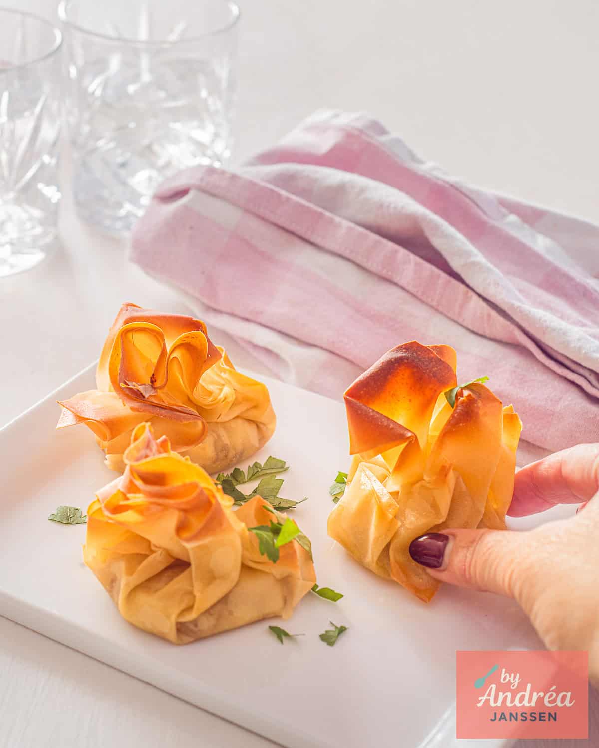 A hand taking one of three Honey Walnut Goat Cheese Phyllo Parcels on a white plate.