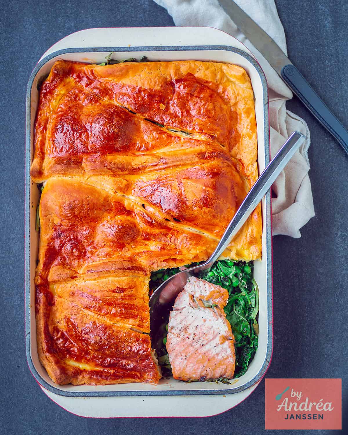 Een foto van bovenaf van een ovenschotel met croissantdeeg, zalm en groene groenten.