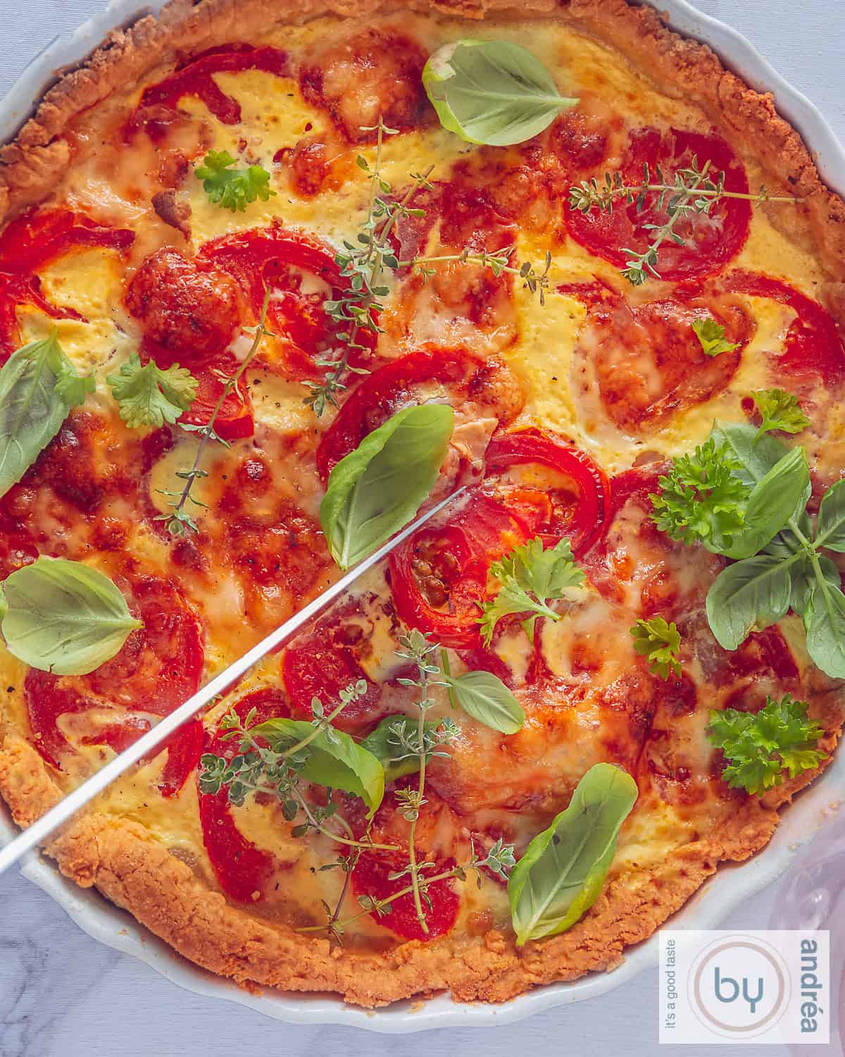 A top-down photo of a quiche with tomato, brie and fresh herbs