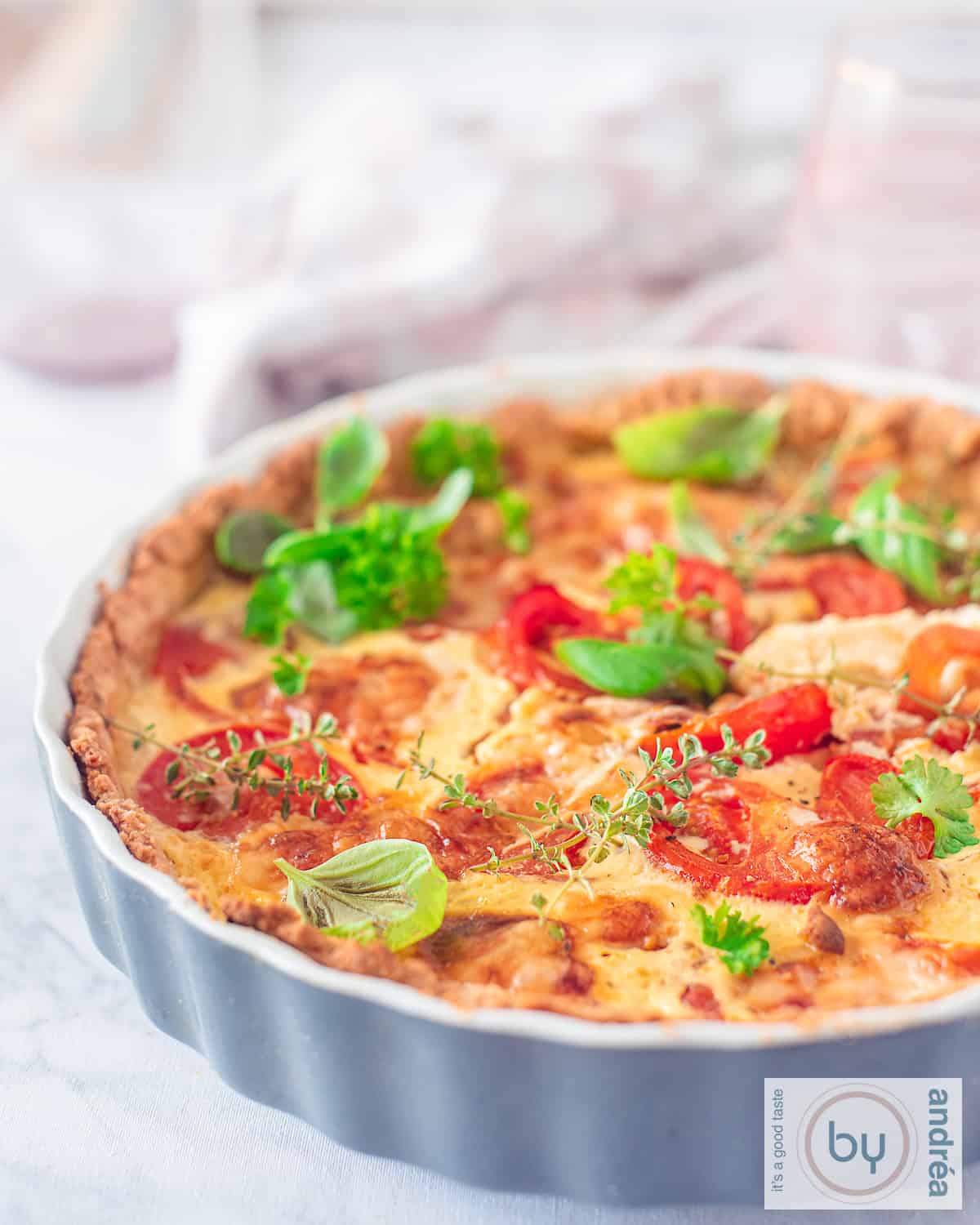 Part of a grey quiche dish filled with a Brie, tomato and green herbs quiche