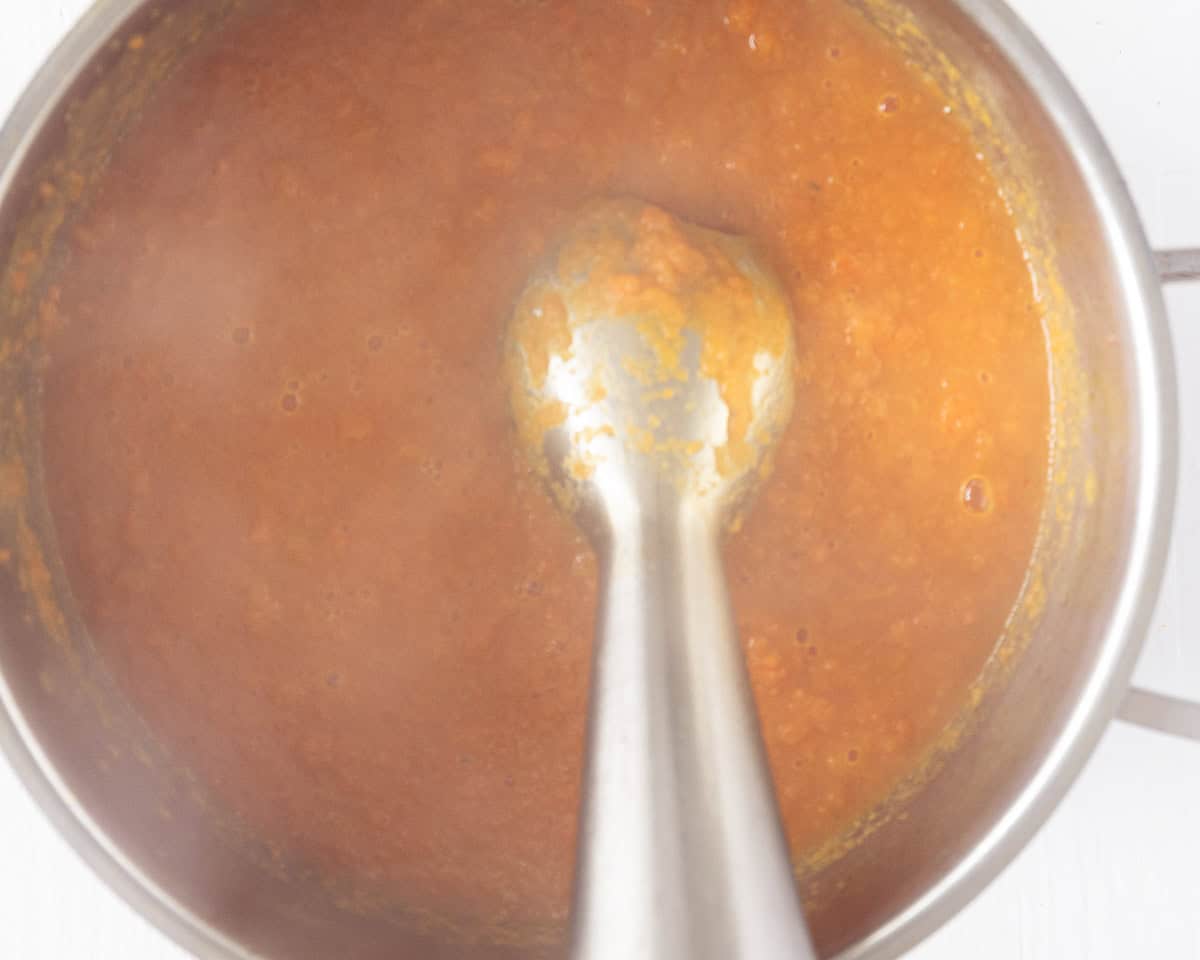 An immersion mixer, mixing the carrot soup until smooth.