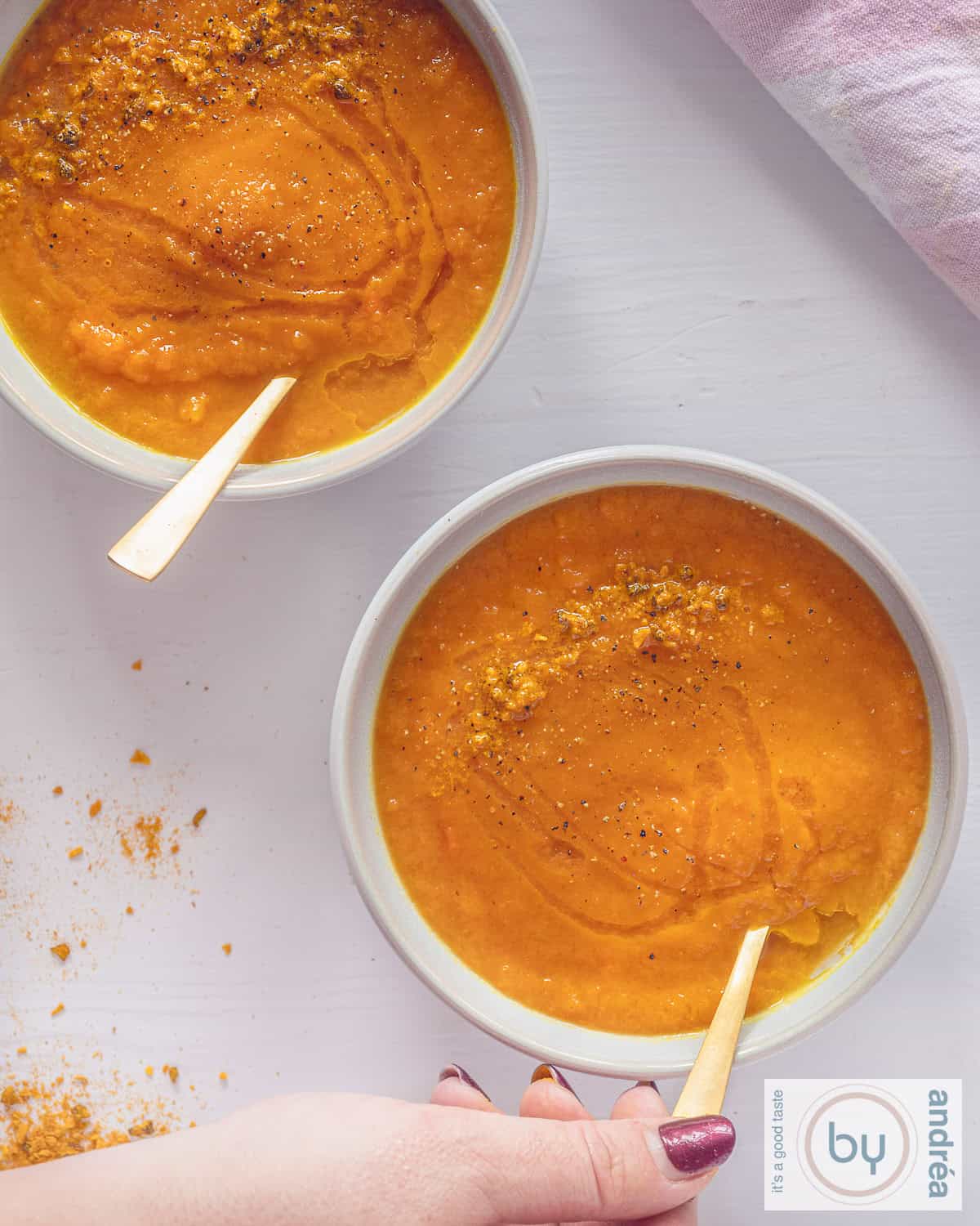 A height picture, top down of two bowls filled with carrot soup with curry spice mix, diagonally alligned.