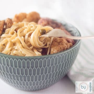 A square photo of a green bowl filled with cauliflower, peas, steak and noodles. A fork with some noodles twisted around it