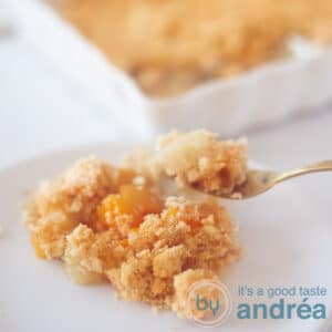 A square photo with a plate with apple, peach and a crumble. In the background a baking dish.