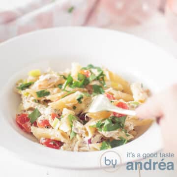 A square photo with a white deep plate filled with pasta, herb cream cheese and smoked mackerel and vegetables. A fork pricks the penne.
