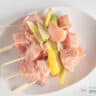 A white plate with five skewers with cubes of salmon, lemon and lime wedges strung on a skewer.