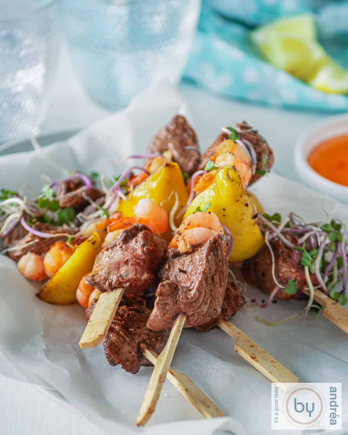 Een hoogtefoto met een witte ondergrond met 5 surf en turf spiesjes, twee glazen en een blauwe doek in de achtergrond