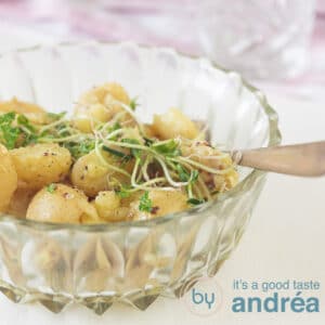 a square photo of a glass bowl filled with potato salad and some greens. A white backdrop and a pink white cloth in the back