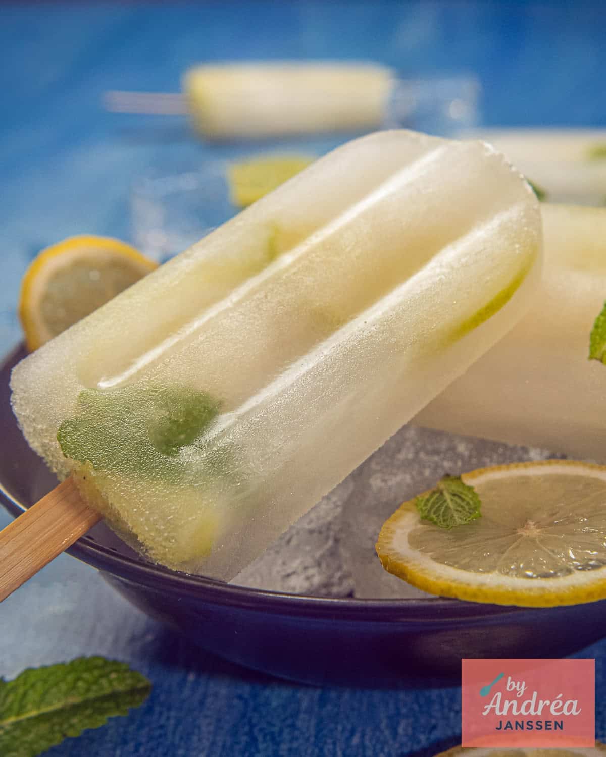 A photo with a black bowl of lemon ice creams with lime and mint on a blue background