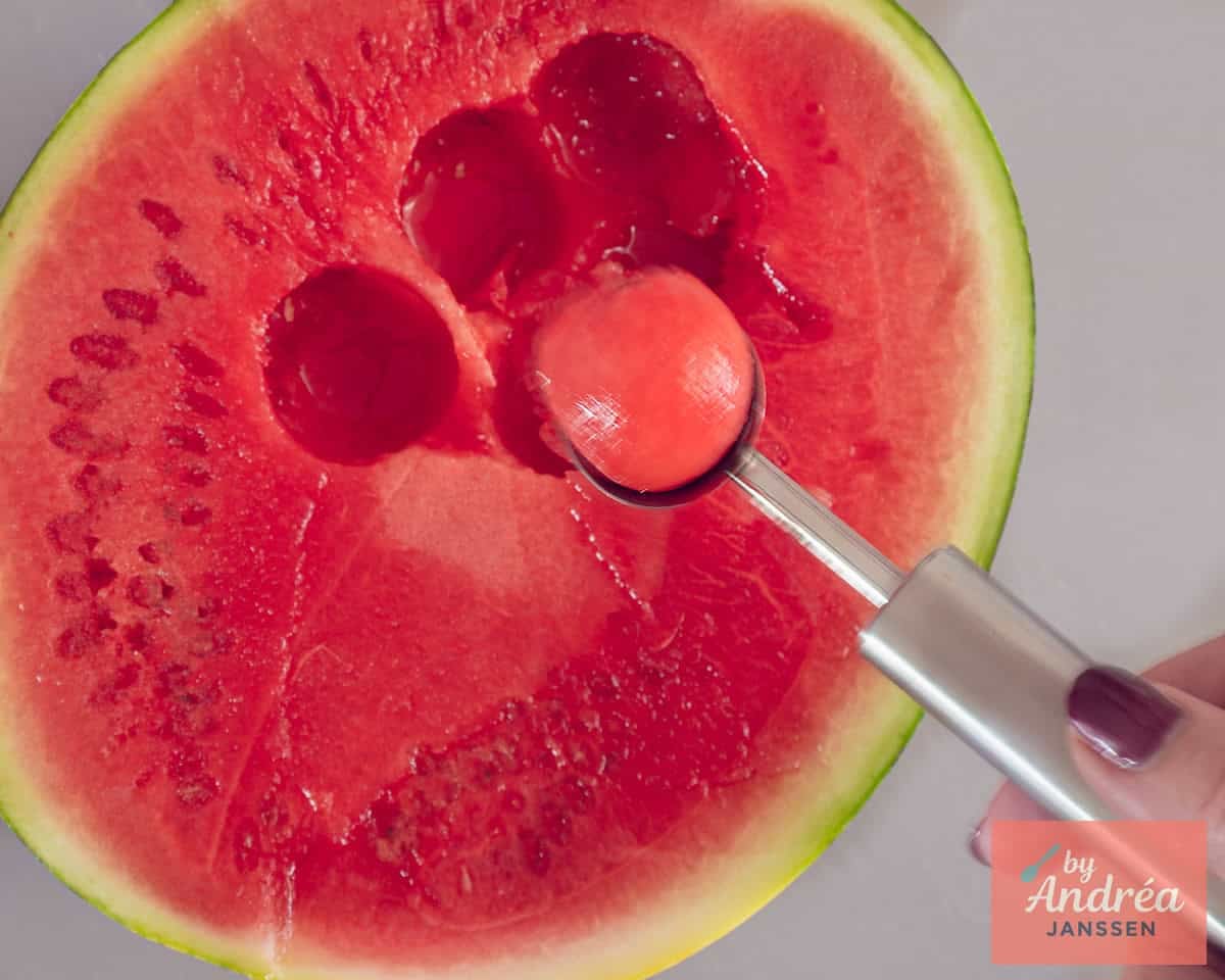 Een meloenschep boven een watermeloen die een balletje vasthoudt.