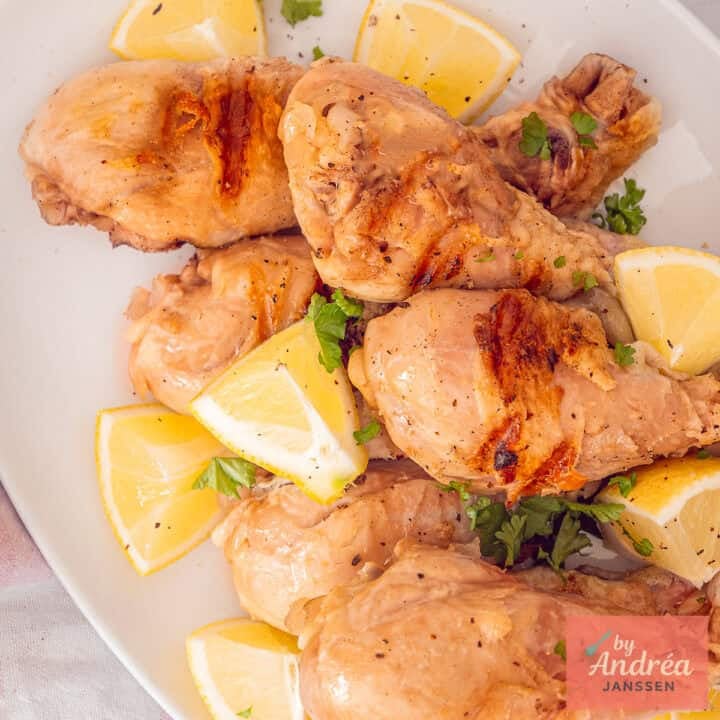 A square photo of a white plate with grilled and pickled drumsticks with lemon.