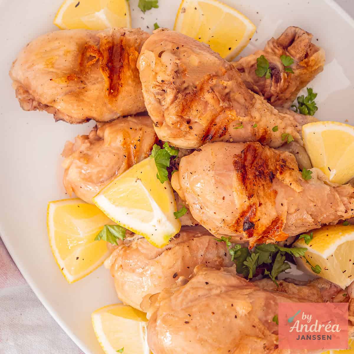 A square photo of a white plate with grilled and pickled drumsticks with lemon.
