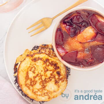A square photo with pancakes and plum compote in a pink dish on a white plate. A golden fork lies above it.