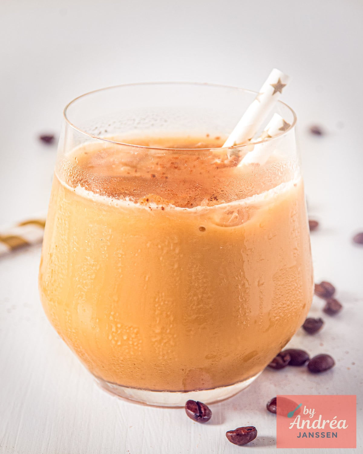 Glass of creamy iced coffee with heavy cream, served with a straw and cocoa powder