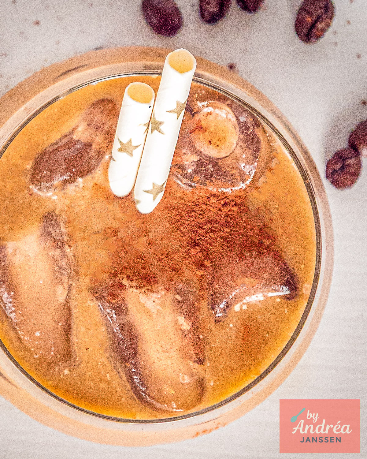 Iced coffee with ice cubes, cocoa powder and two straws seen from above