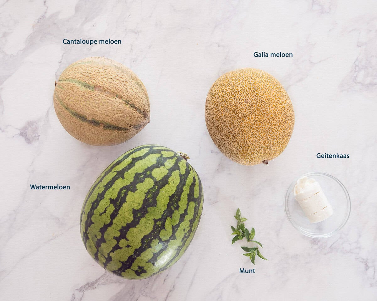 Ingredienten Meloensalade Met Geitenkaas En Munt op een witte marmeren achtergrond met een tekstbeschrijving.