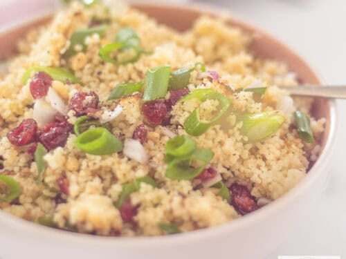 A square photo of a bowl of couscous with pine nuts, lemon and cranberries
