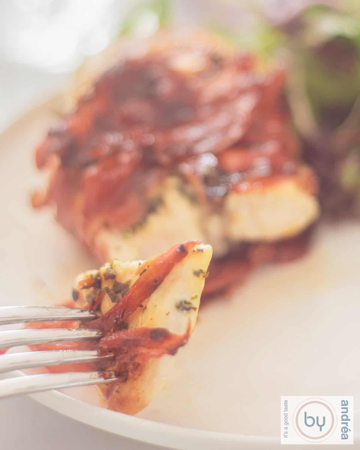 Een kipfilet met Serranoham en Italiaanse kruiden op een wit bord. Een stukje erafgesneden.