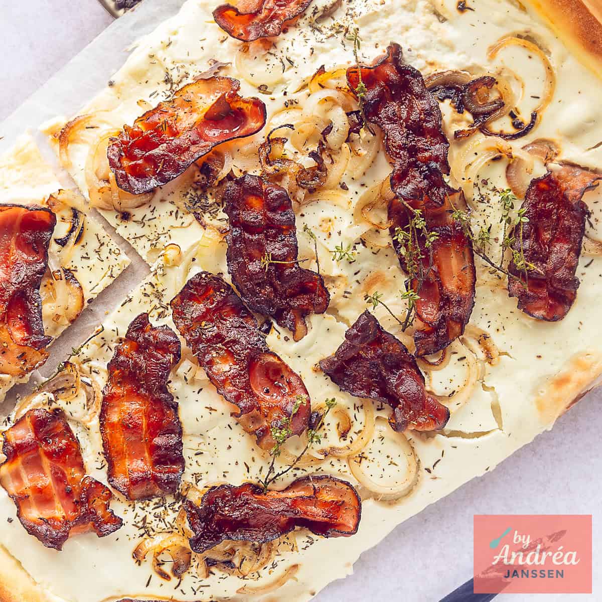 A square photo showing part of a flamkuchen with crème fraîche topping, bacon, thyme and onions.