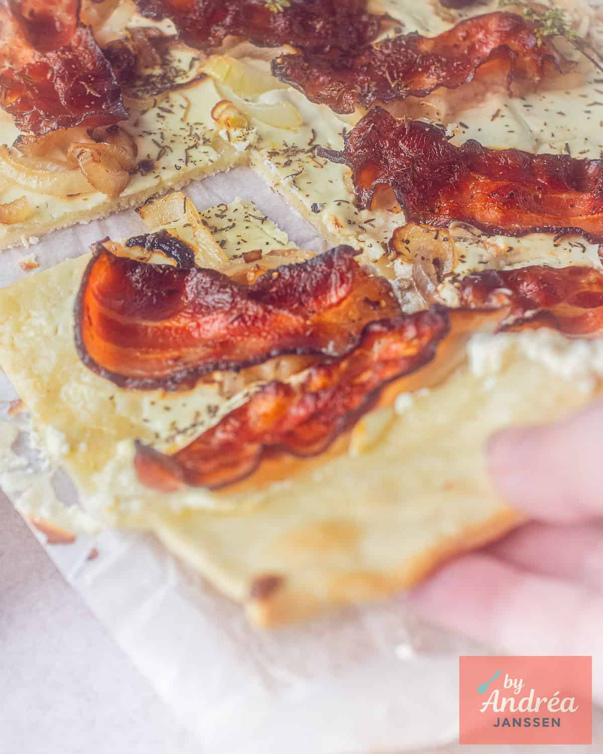 A hand takes a piece of flammkuchen with bacon, onion and thyme
