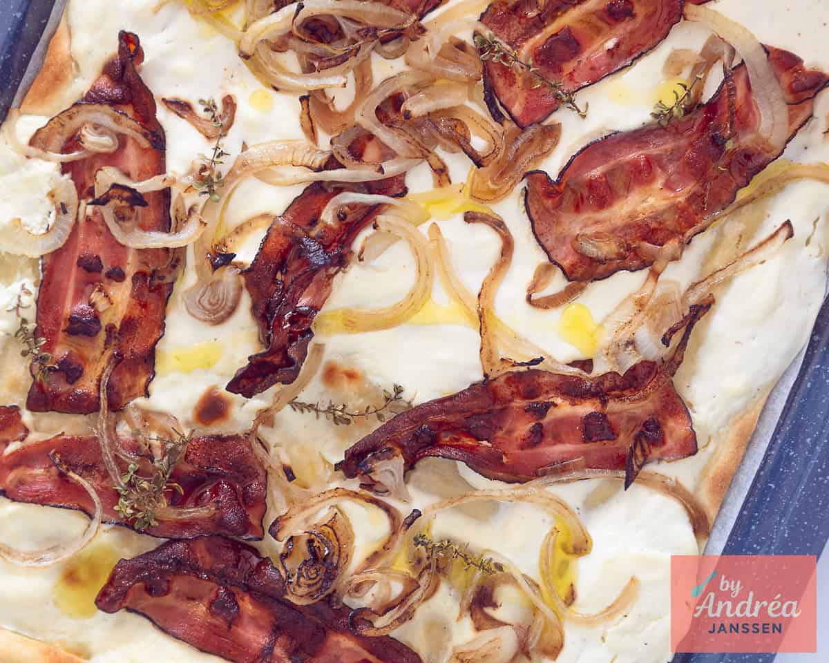 Flammkuchen with bacon, onion and thyme on a baking tray.