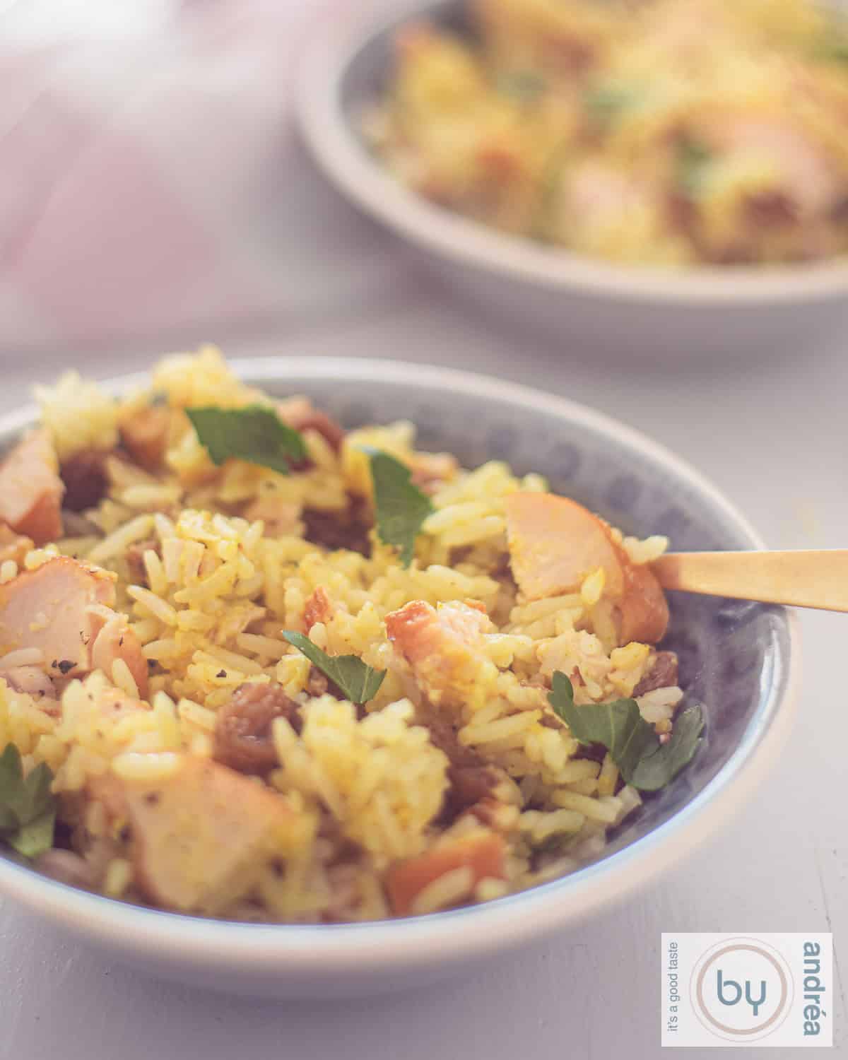 A portion of a gray bowl of curry rice with chicken, parsley, walnuts and raisins as a salad.