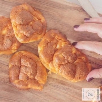 A square photo with a wooden board with cloud breads on it. A hand grabs an oopsie