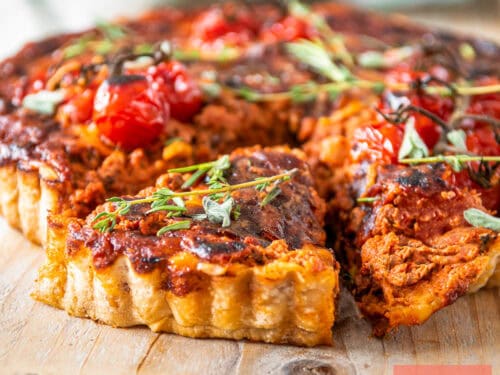A square photo of a bolognese quiche with a slice cut out of it.