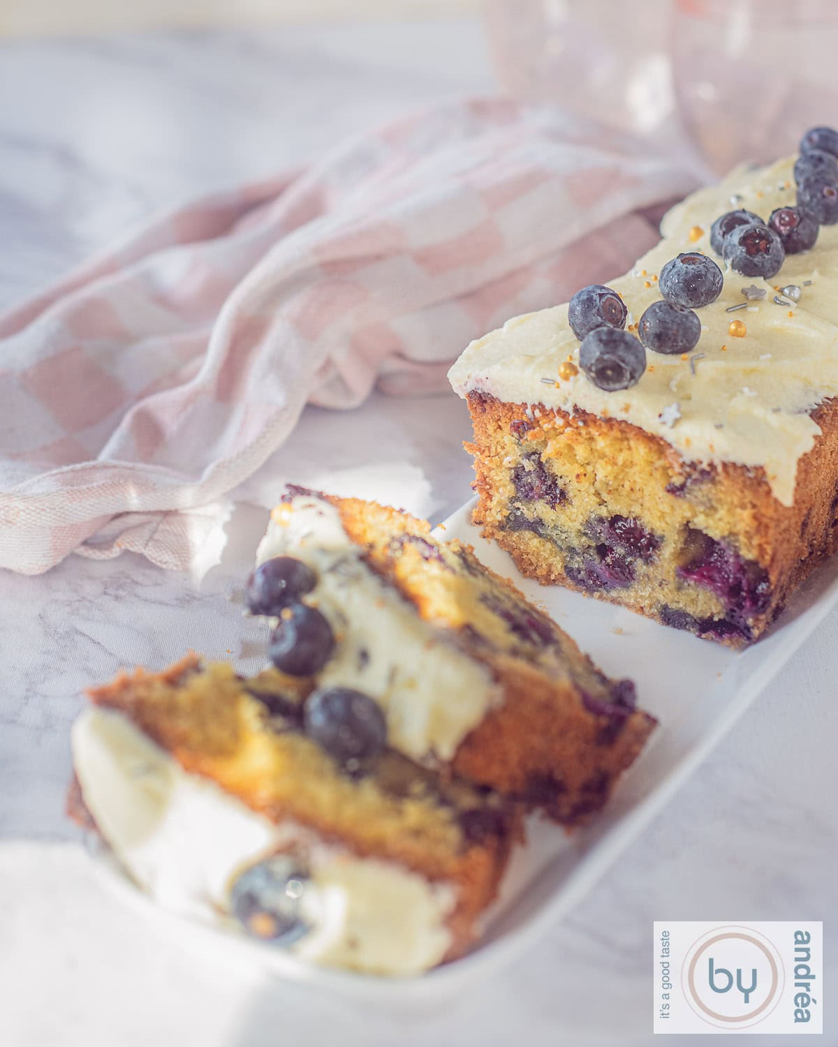 A height photo of a blueberry cake with vanilla frosting from which two slices have been cut.