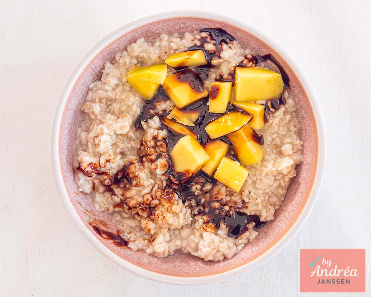 A pink bowl with oatmeal, date syrup, and mango