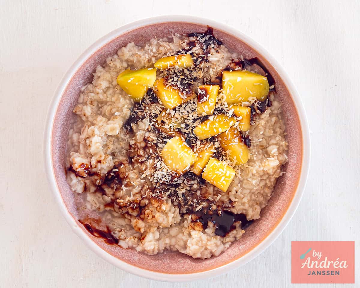 A pink bowl with oatmeal, mango, date syrup, and coconut
