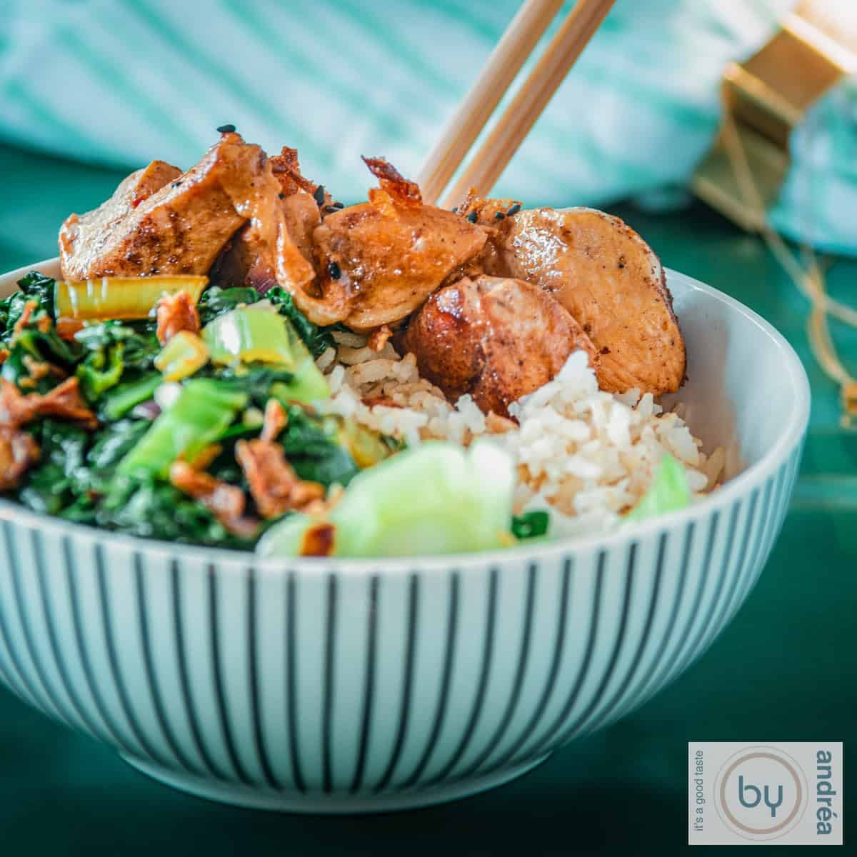 A square photo with a white striped bowl containing bok choy, rice and sticky ketjap chicken.