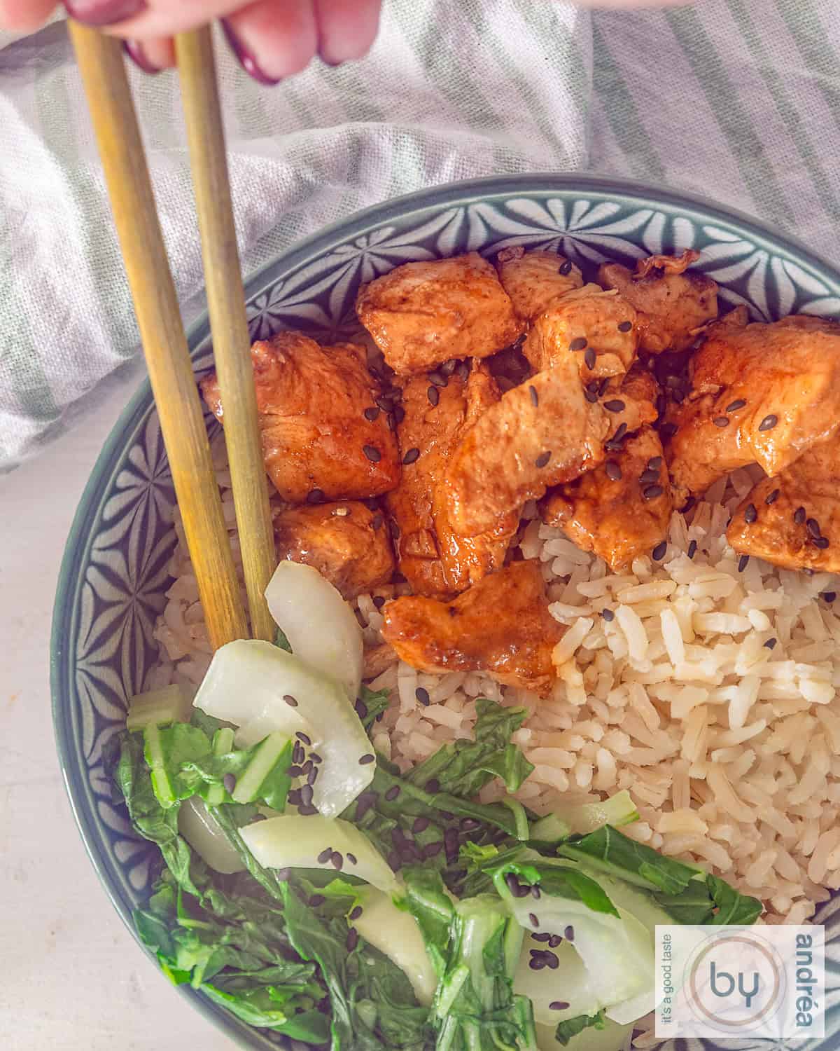 An overhead photo of a bowl of sticky ketjap chicken, bok choy, and lemon rice. Two chopsticks are in the bowl.