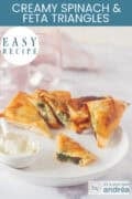 Part of a white plate with bites of filo pastry, spinach and feta. A dip in front and half a bite through which you can see the filling. Above a text: easy recipe, Crispy Spinach & Feta Triangles
