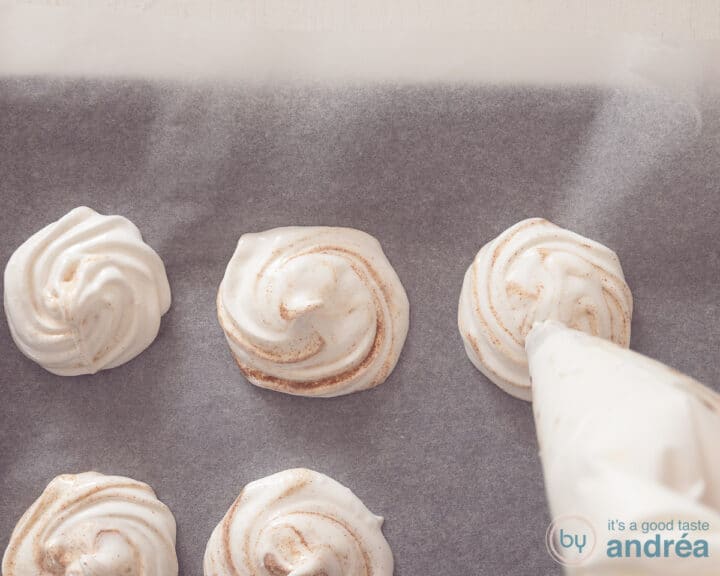 A piping bag makes mounds of gingerbread foam on baking paper.