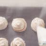 A piping bag makes mounds of gingerbread foam on baking paper.