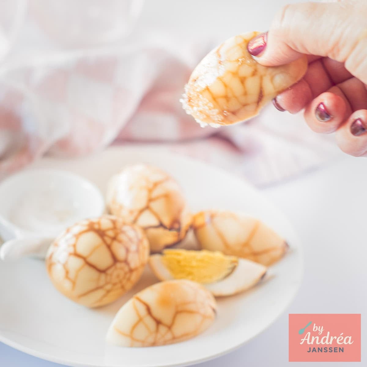 A square picture with tea eggs on a plate, some quartered, and a hand picking one of them.