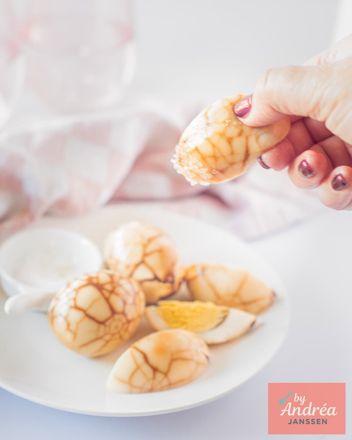 A white plate with tea eggs, a hand picking one dipped in salt.
