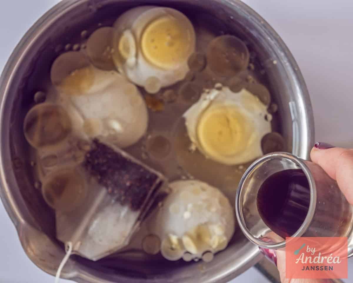 A saucepan with eggs where tea and soy sauce and sesame oil are added