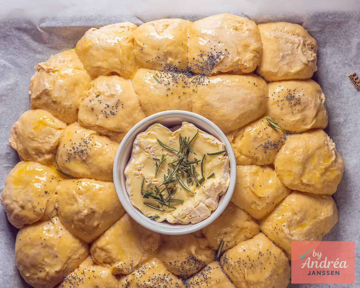 In the center, a ramekin with camembert and rosemary, surrounded by dough balls topped with poppy seeds.