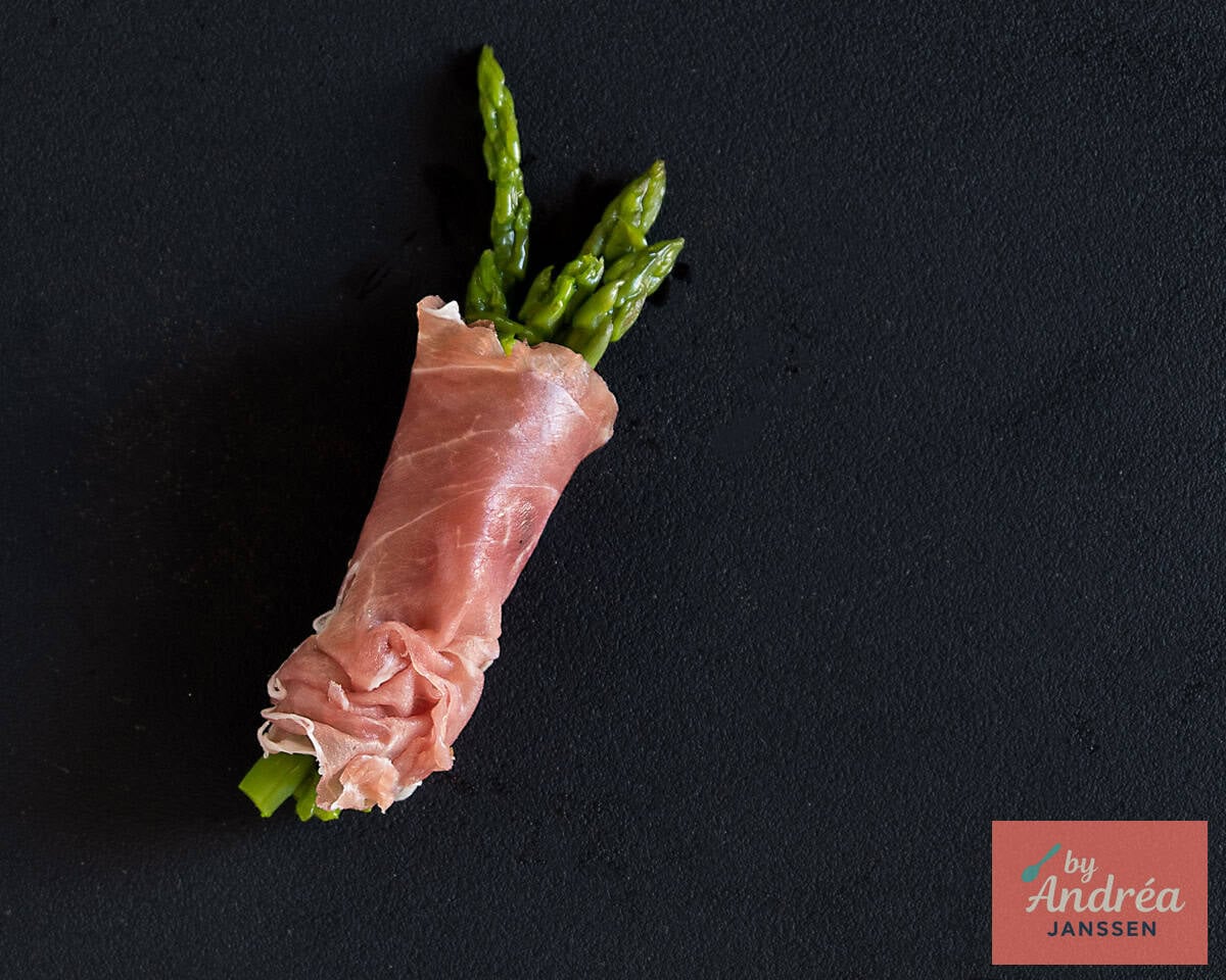 Green asparagus wrapped in Parma ham on a black background